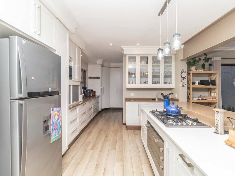 A well-appointed kitchen featuring white cabinetry, stone countertops, a gas hob, built-in oven, and modern laminate flooring with ample storage space.