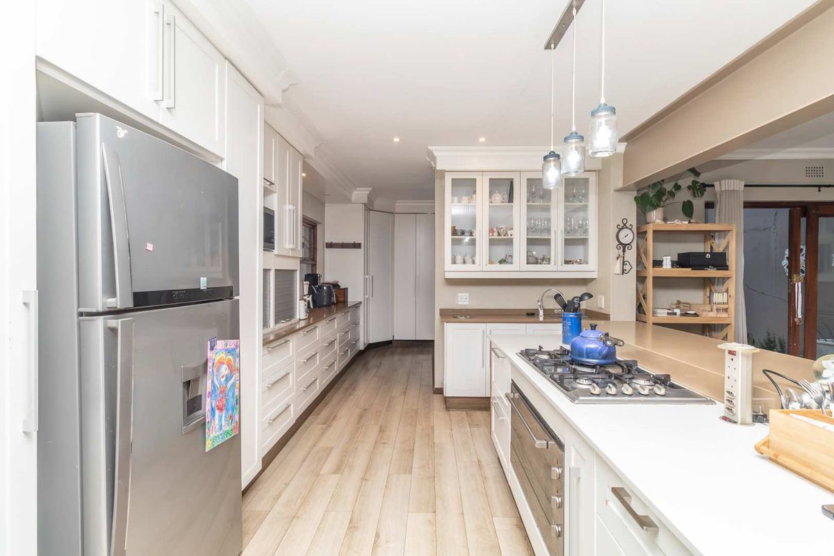 A well-appointed kitchen featuring white cabinetry, stone countertops, a gas hob, built-in oven, and modern laminate flooring with ample storage space.