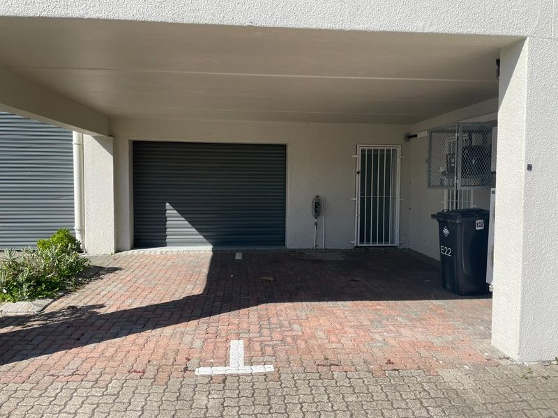 A covered parking area featuring a roller shutter garage door, security gate, and paved driveway, providing secure access to the property.