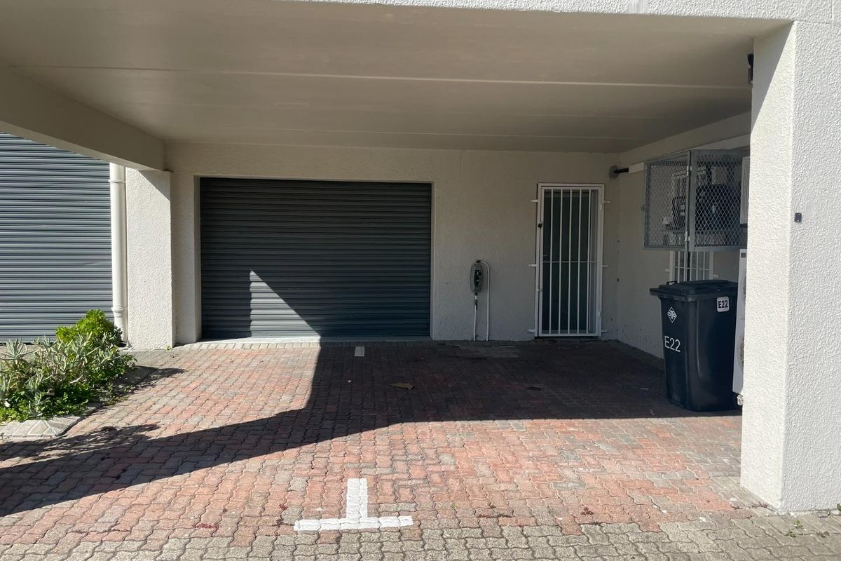 A covered parking area featuring a roller shutter garage door, security gate, and paved driveway, providing secure access to the property.