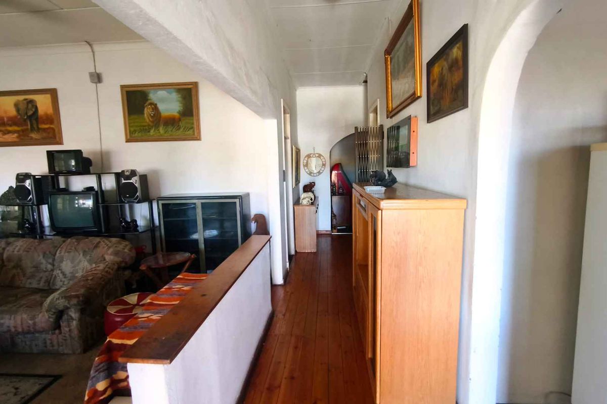 A living area featuring timber flooring, an arched doorway, and an exposed ceiling beam, providing a traditional layout with potential for modernization.