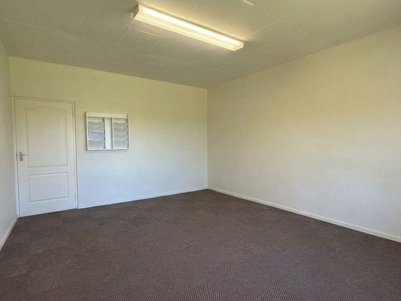 A clean, empty office space featuring neutral walls, carpeted flooring, and a wall-mounted document rack, suitable for a professional workspace.