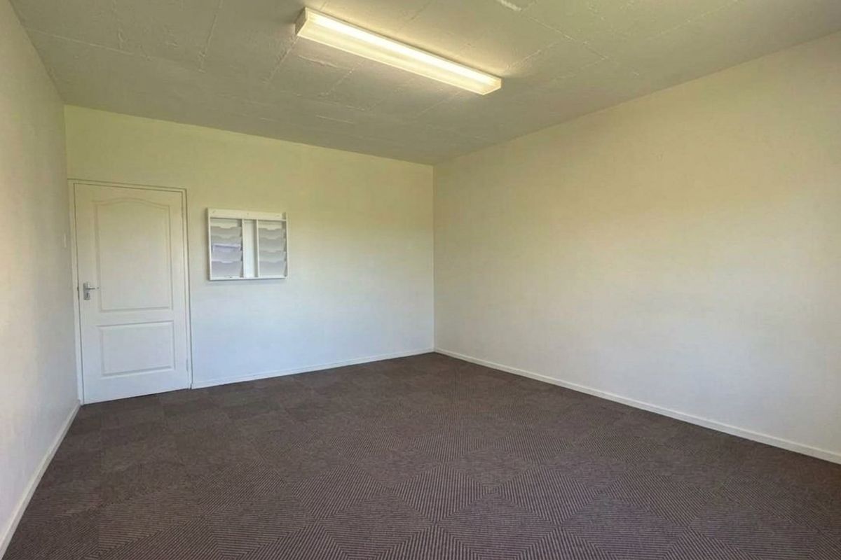 A clean, empty office space featuring neutral walls, carpeted flooring, and a wall-mounted document rack, suitable for a professional workspace.