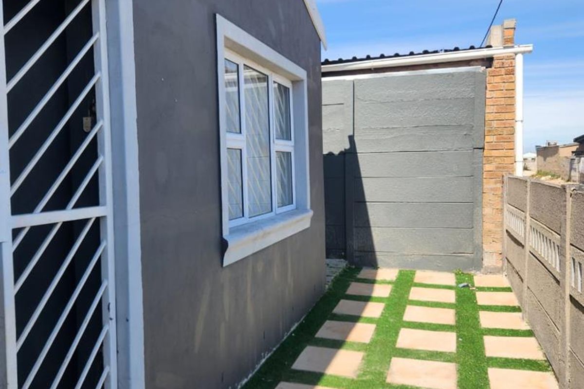 A side exterior view of the property featuring a paved walkway with grass inserts, a security gate, and a precast concrete boundary wall.