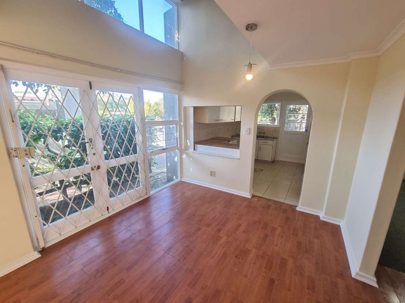 Open plan living area with double volume ceilings, laminate flooring, and a serving hatch connecting to the kitchen.