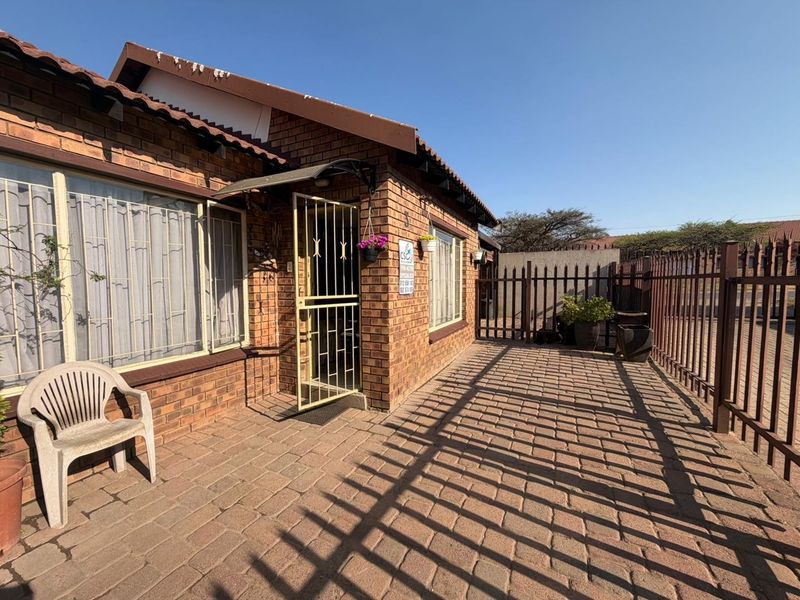 Front exterior view of a face brick house featuring a paved entrance area, security gate, and metal perimeter fencing.