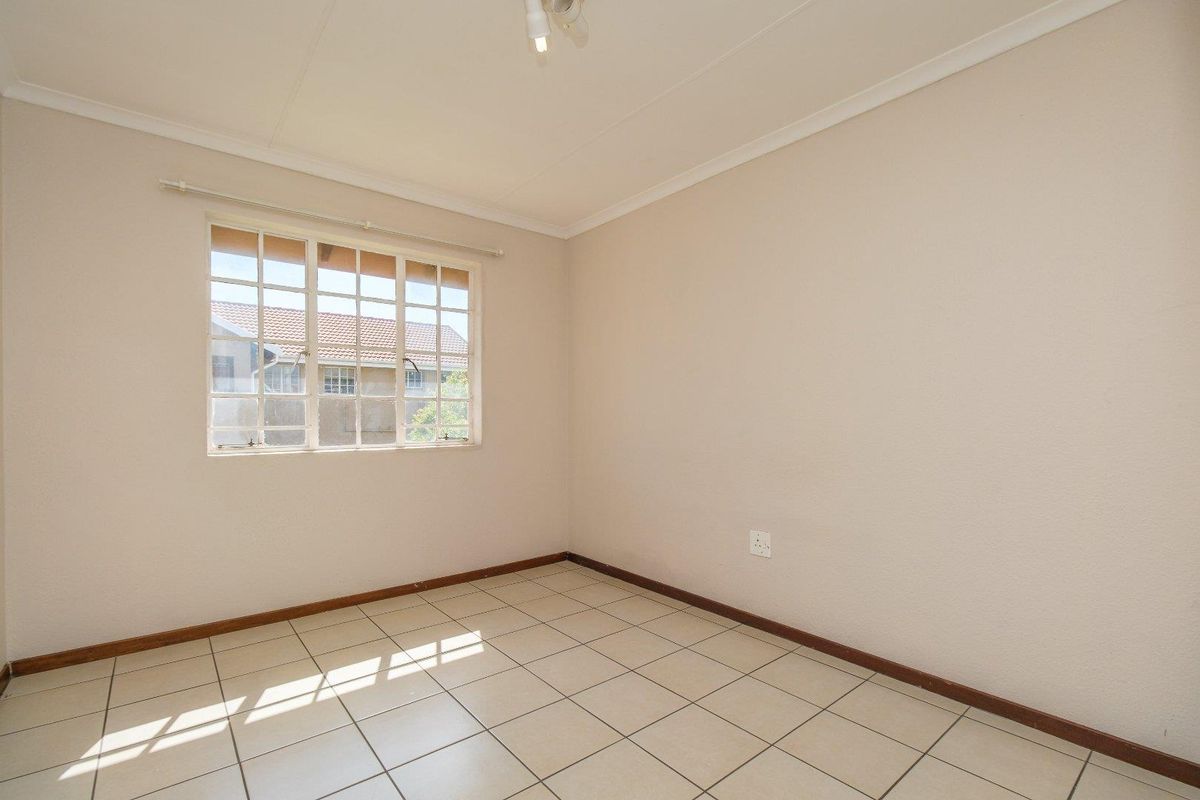 A bright, empty bedroom featuring neutral tiled flooring, coved ceilings, and a grid-pattern window allowing for natural light.