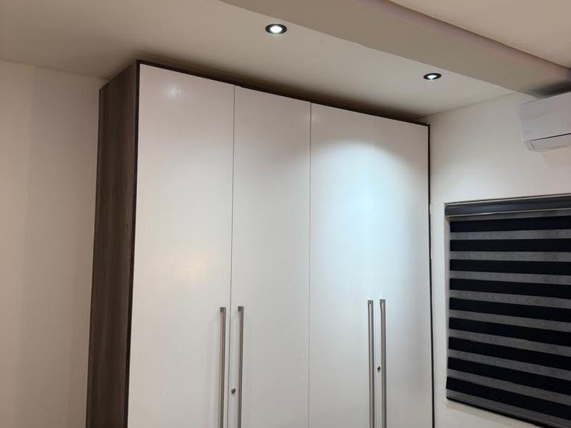 A well-maintained bedroom featuring a modern built-in wardrobe, recessed ceiling lighting, and a wall-mounted split-system air conditioning unit.