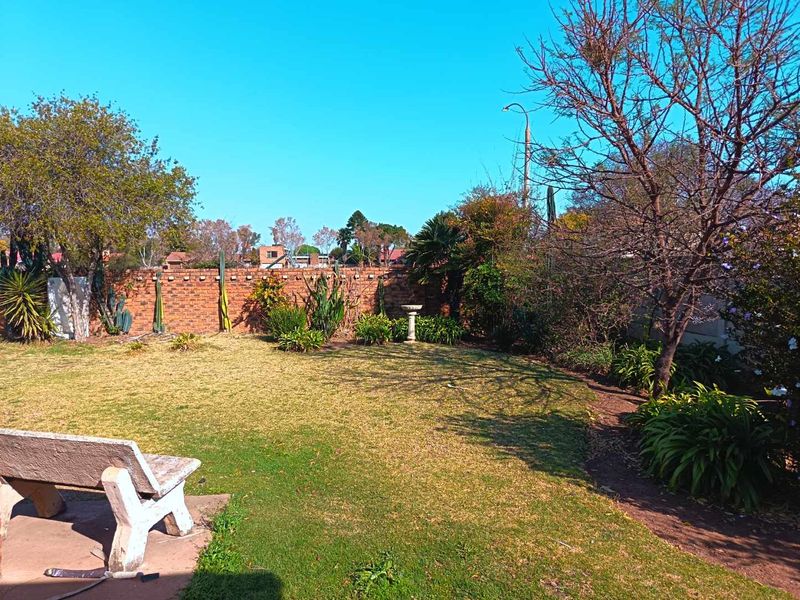 A private backyard garden featuring a lawn, established trees, and a brick boundary wall with a concrete bench and bird bath.