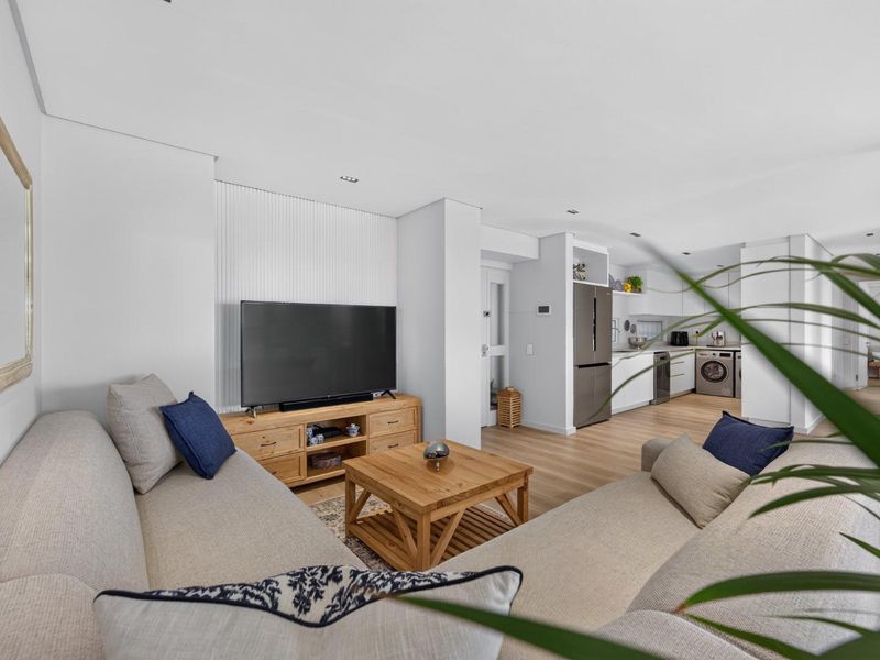Modern open-plan living area featuring light laminate flooring, a slatted feature wall, and a sleek, integrated kitchen with laundry facilities.