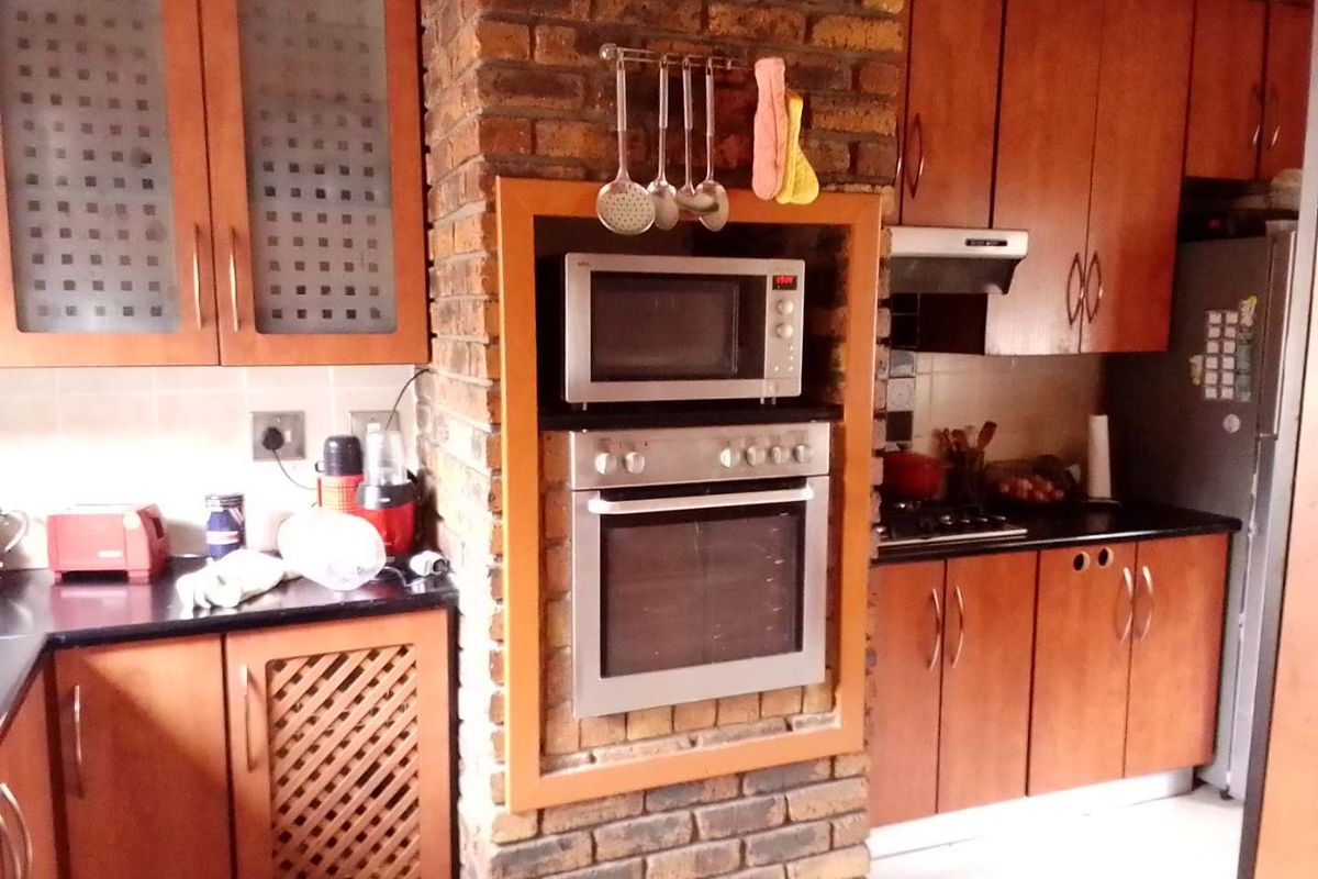A kitchen featuring wooden cabinetry, a built-in oven and microwave set into a rustic brick pillar, and dark countertops.