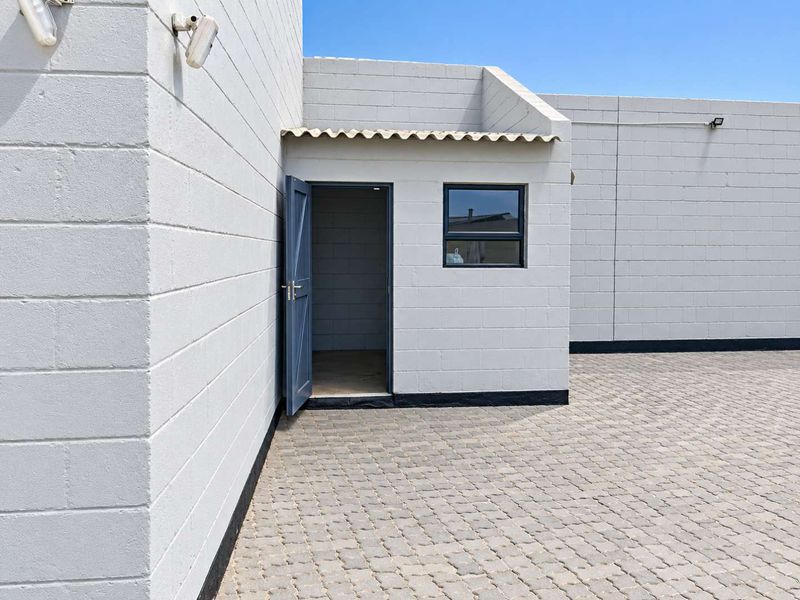 A clean exterior rear courtyard featuring concrete block walls, paved flooring, and a secure entrance door with an adjacent aluminium window.