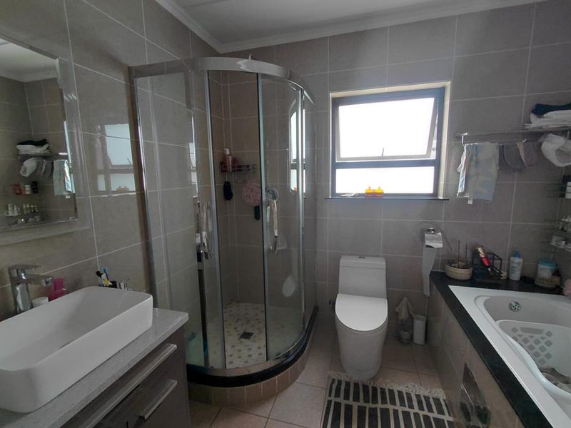 Modern bathroom featuring a corner shower enclosure, built-in bathtub, vanity with vessel sink, and neutral wall tiling.