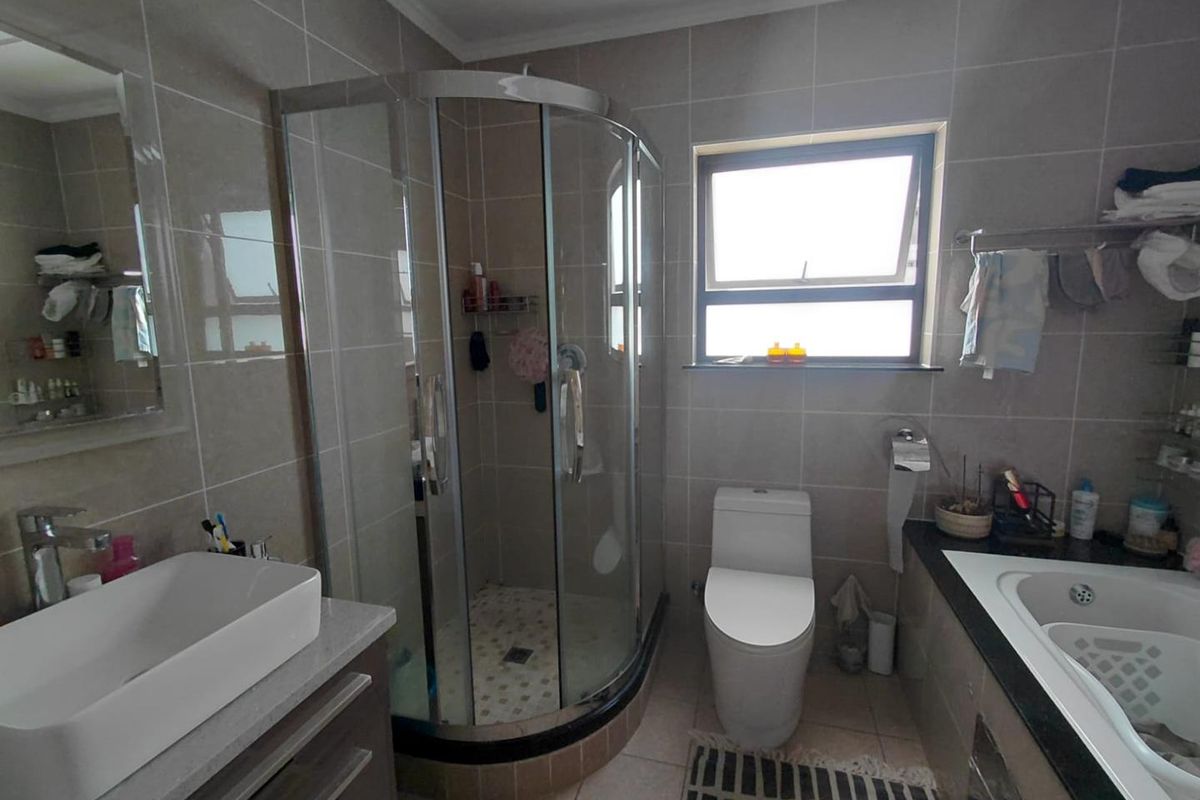 Modern bathroom featuring a corner shower enclosure, built-in bathtub, vanity with vessel sink, and neutral wall tiling.