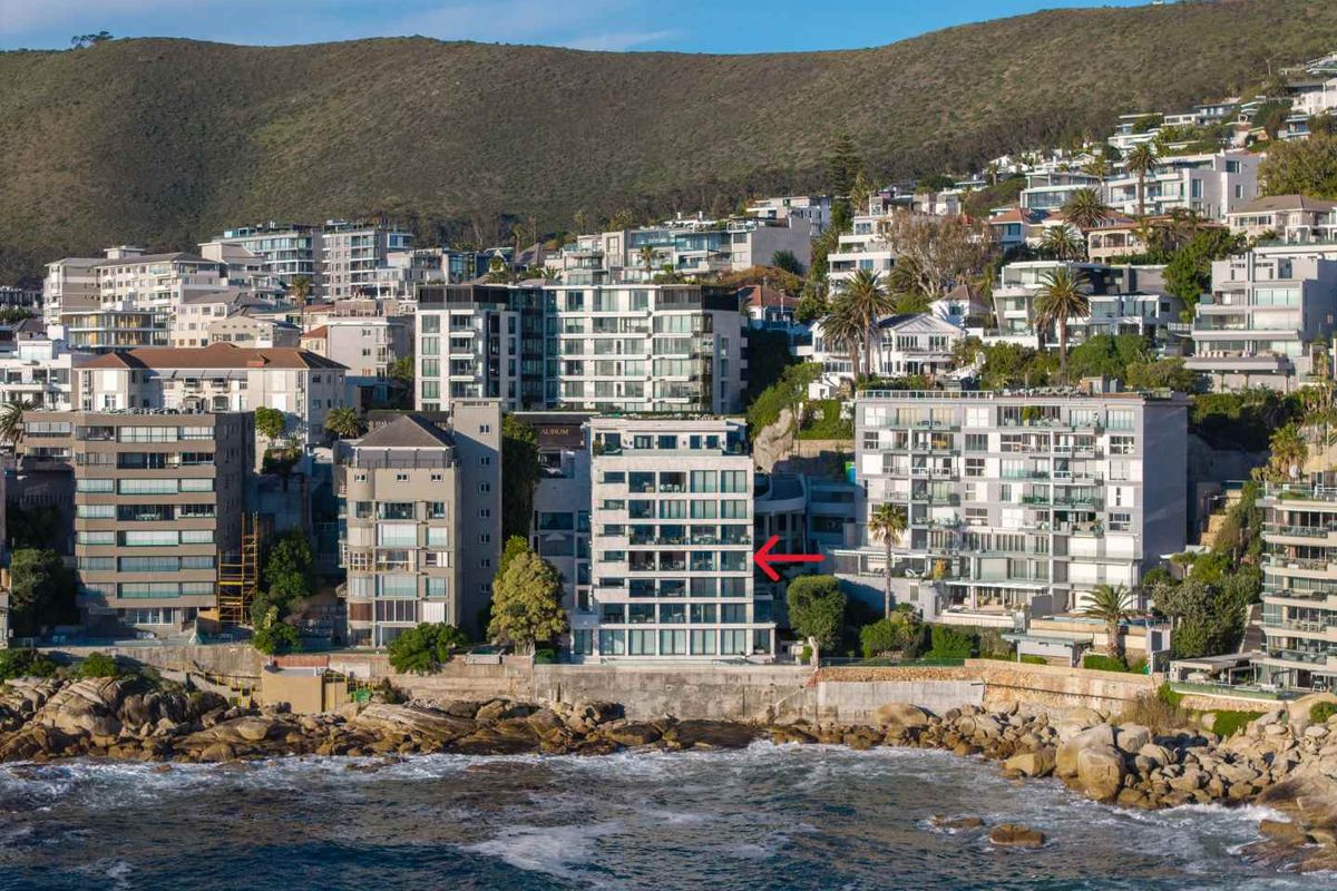 Aerial view of a modern multi-story apartment building situated on the coastline, highlighting its prime location and architectural presence.