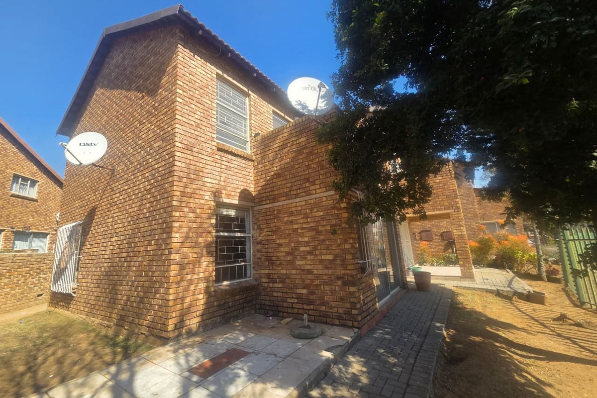 Rear view of a face brick apartment building featuring paved walkways, security bars on windows, and satellite dish installations.