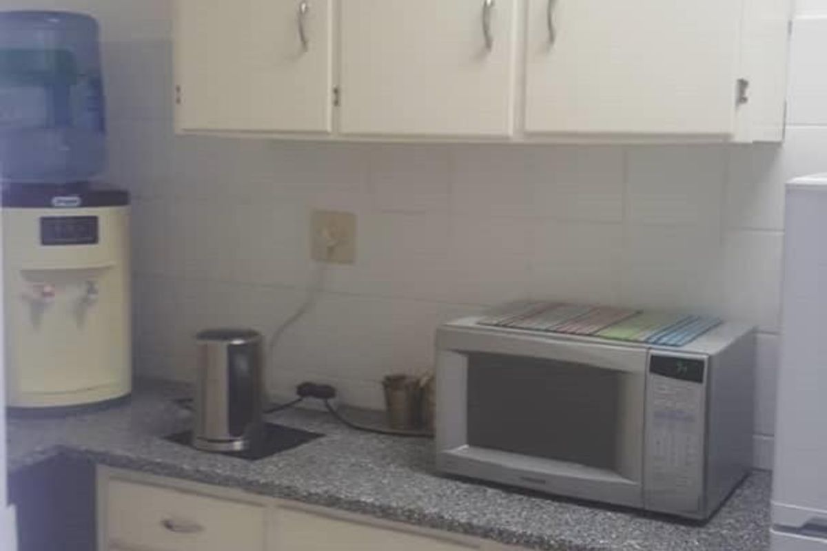 A compact office kitchenette featuring white built-in cabinetry, a durable laminate countertop, and a tiled backsplash.