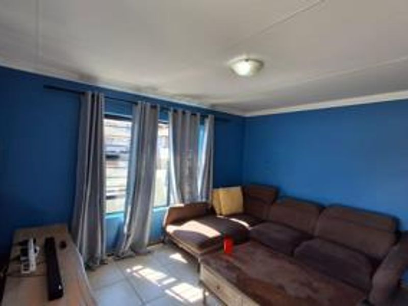 A living room featuring tiled flooring, blue painted walls, and a window fitted with security bars.