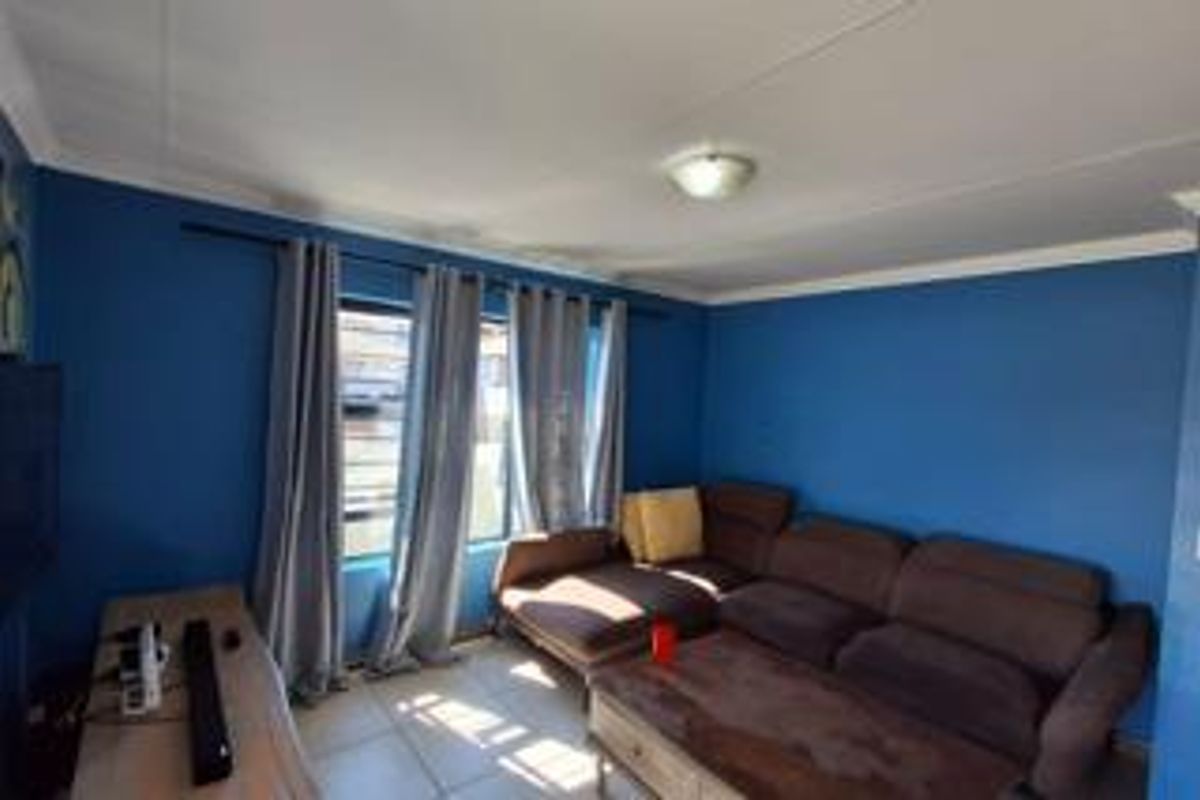 A living room featuring tiled flooring, blue painted walls, and a window fitted with security bars.