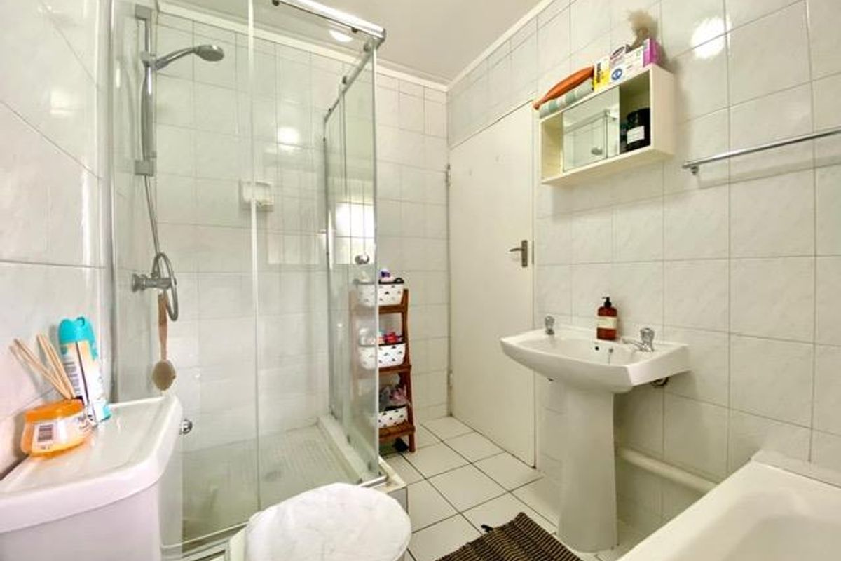 A functional bathroom featuring a glass-enclosed shower, pedestal sink, and bathtub with white wall tiling throughout.