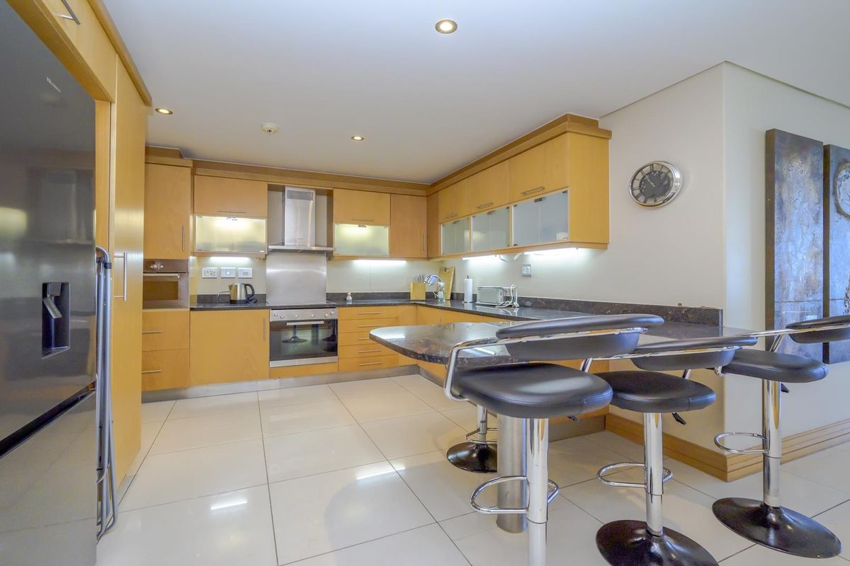 A well-maintained kitchen featuring light wood cabinetry, granite countertops, integrated appliances, and a functional breakfast bar with tiled flooring.
