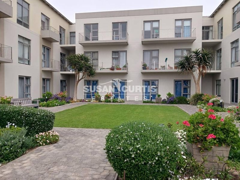 A well-maintained retirement village courtyard featuring a central lawn, landscaped garden beds, and multi-level apartment units with private balconies.