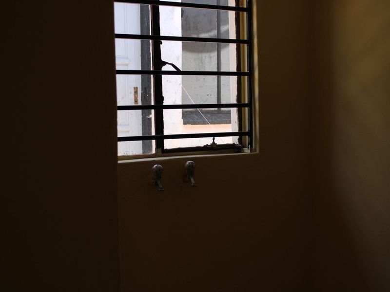 A utility or laundry area featuring wall-mounted taps and a window with security bars, requiring maintenance and repair.