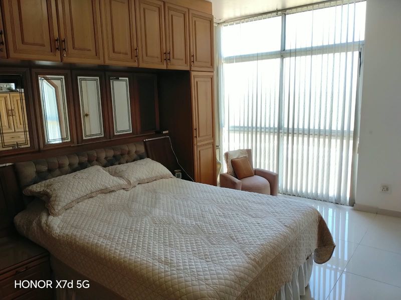 Bedroom featuring extensive built-in wooden cabinetry, large floor-to-ceiling windows with vertical blinds, and polished tiled flooring.