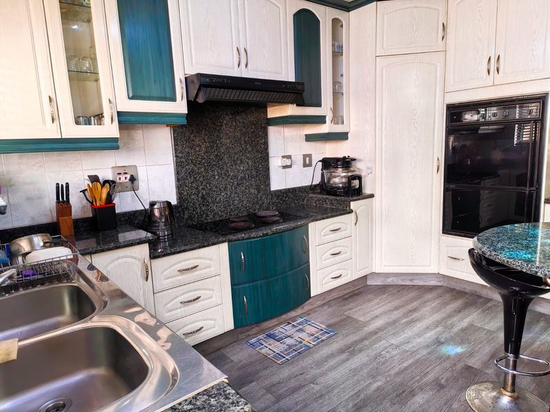 A functional kitchen featuring granite countertops, built-in oven, electric hob, extractor fan, and ample fitted cabinetry with a modern laminate floor finish.