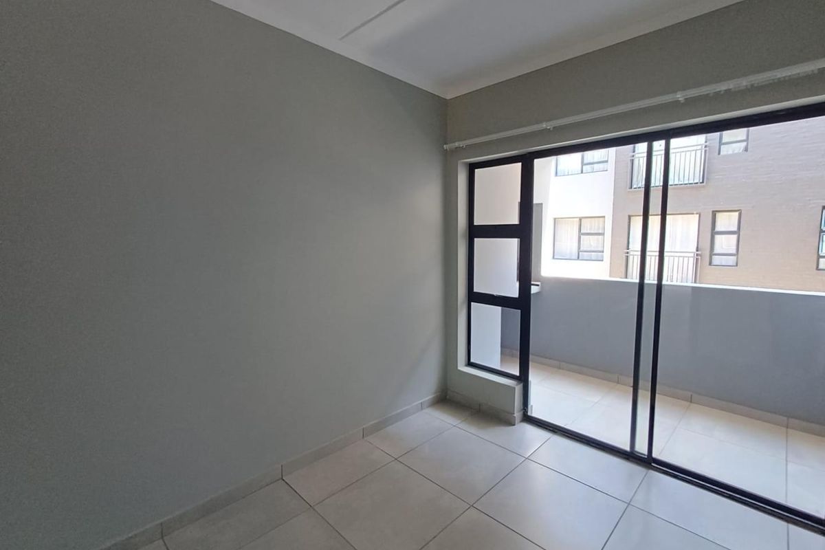 A bright, empty bedroom featuring neutral tiled flooring and large sliding glass doors that open onto a private balcony.