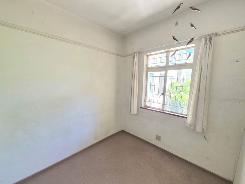 An empty bedroom featuring carpet flooring, a window with security bars, and a traditional picture rail, ready for renovation or staging.