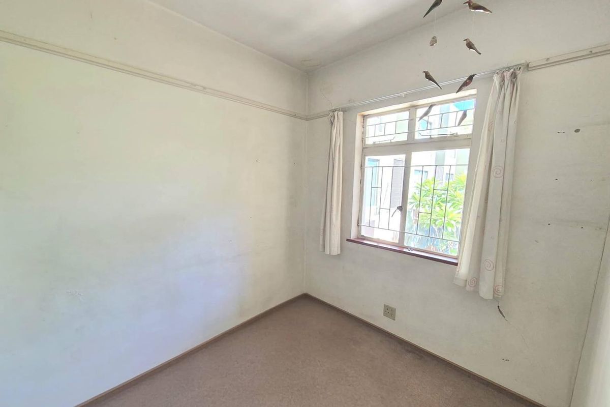 An empty bedroom featuring carpet flooring, a window with security bars, and a traditional picture rail, ready for renovation or staging.