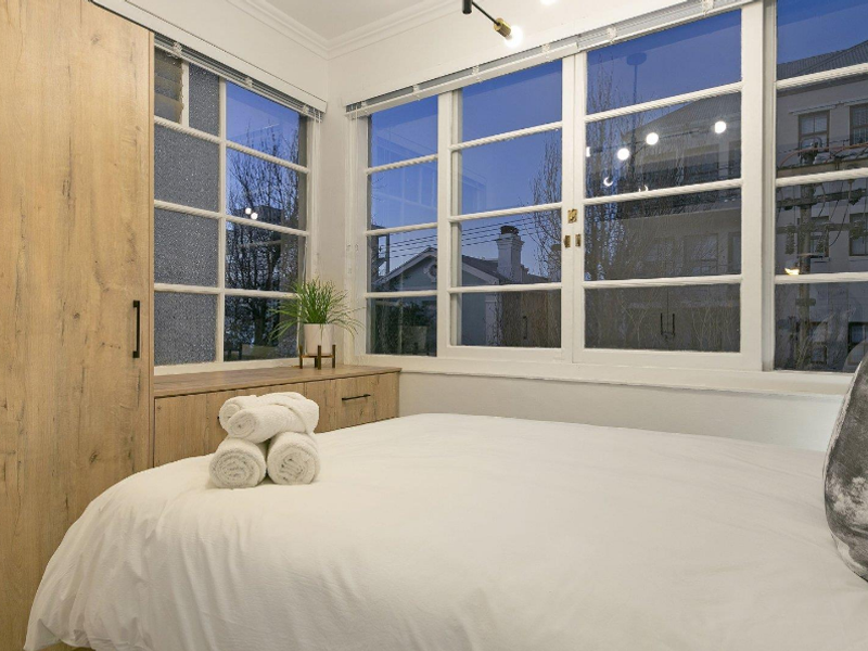 A bright bedroom featuring built-in wood-finish cabinetry and a wardrobe, complemented by large multi-pane windows that provide ample natural light.