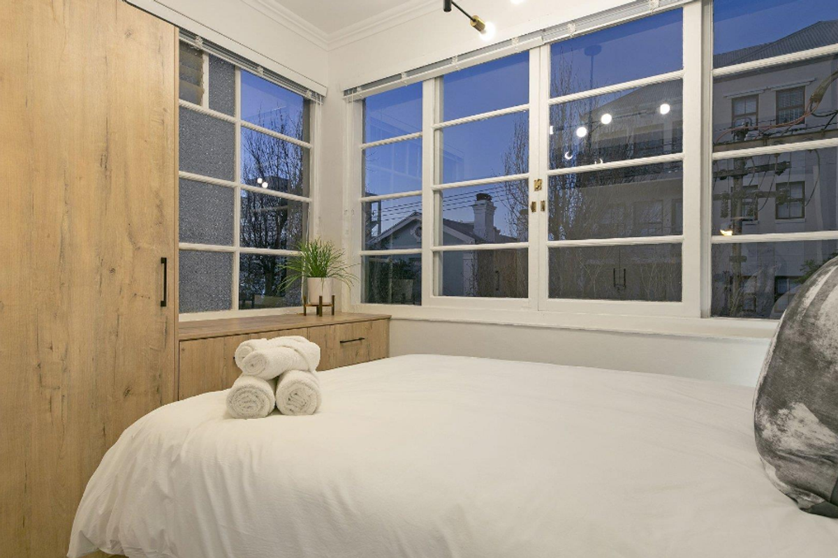 A bright bedroom featuring built-in wood-finish cabinetry and a wardrobe, complemented by large multi-pane windows that provide ample natural light.