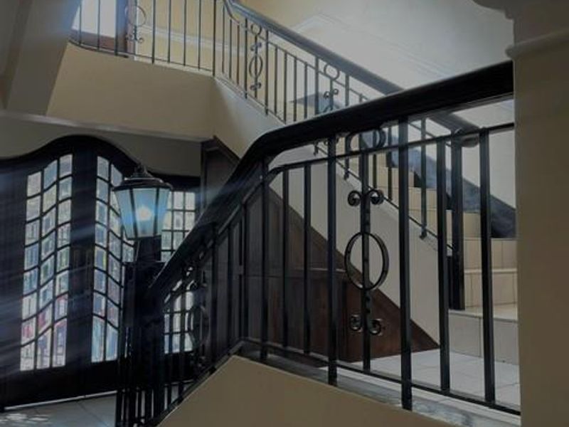 A spacious entrance foyer featuring a grand staircase with wrought iron railings, tiled flooring, and a decorative arched front door.