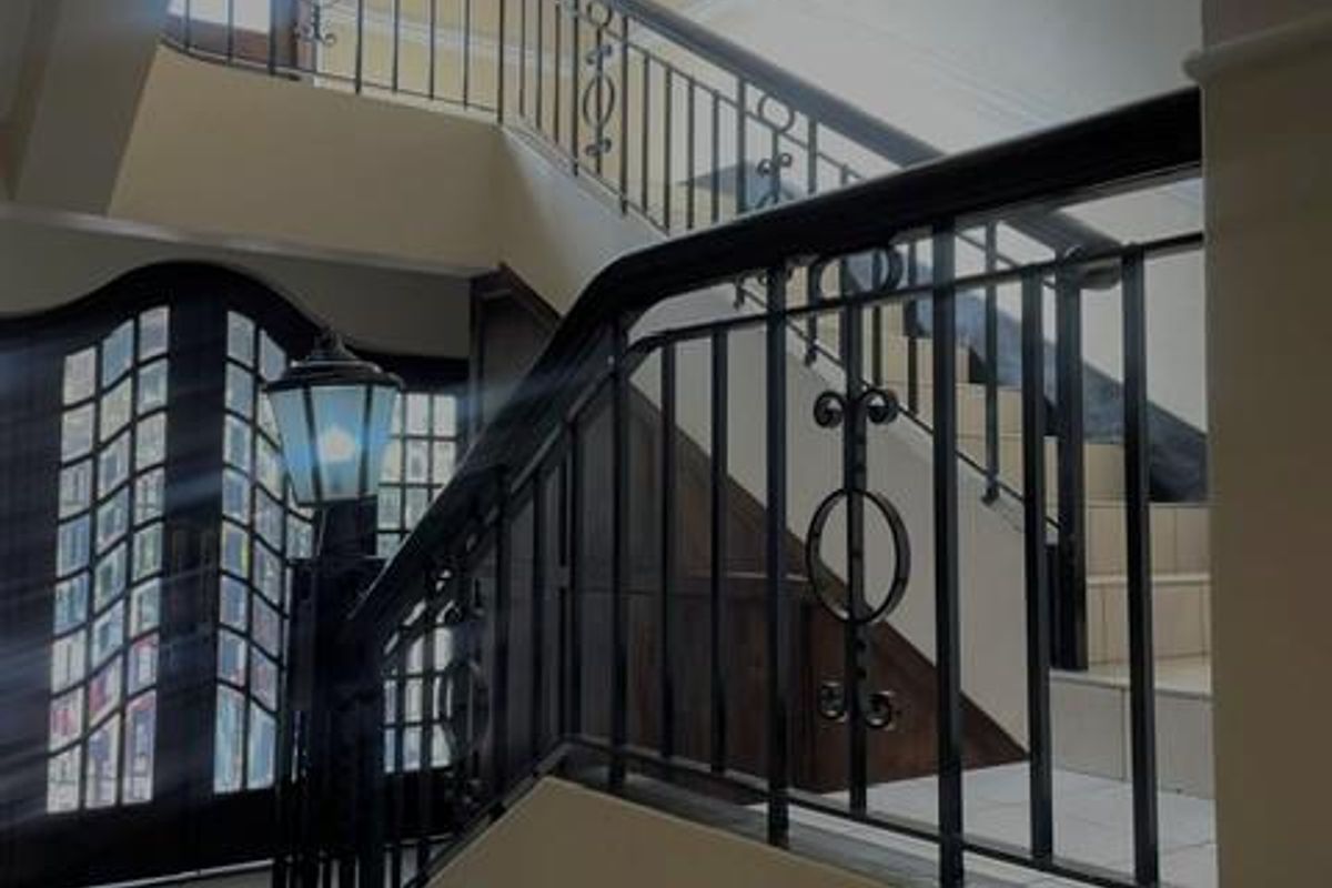 A spacious entrance foyer featuring a grand staircase with wrought iron railings, tiled flooring, and a decorative arched front door.