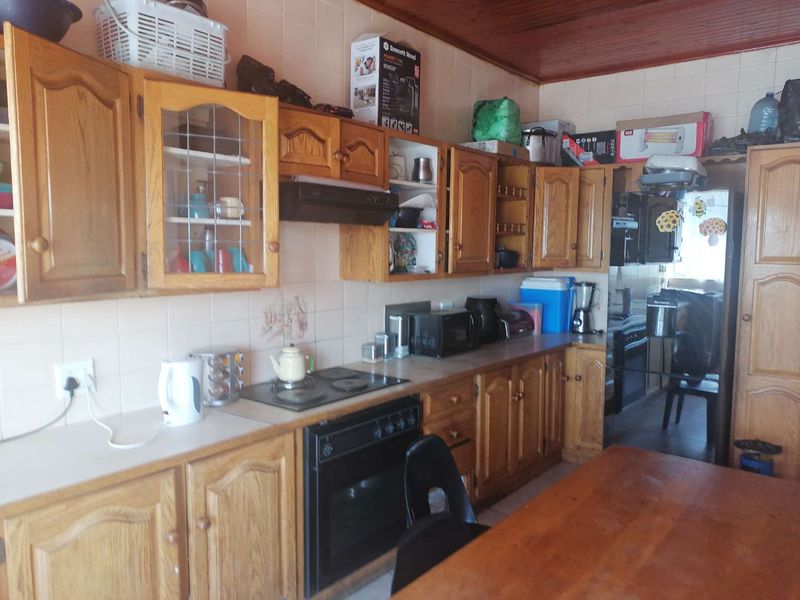 A dated kitchen featuring wooden cabinetry, built-in oven, electric hob, extractor fan, and a timber ceiling, offering potential for a modern renovation.