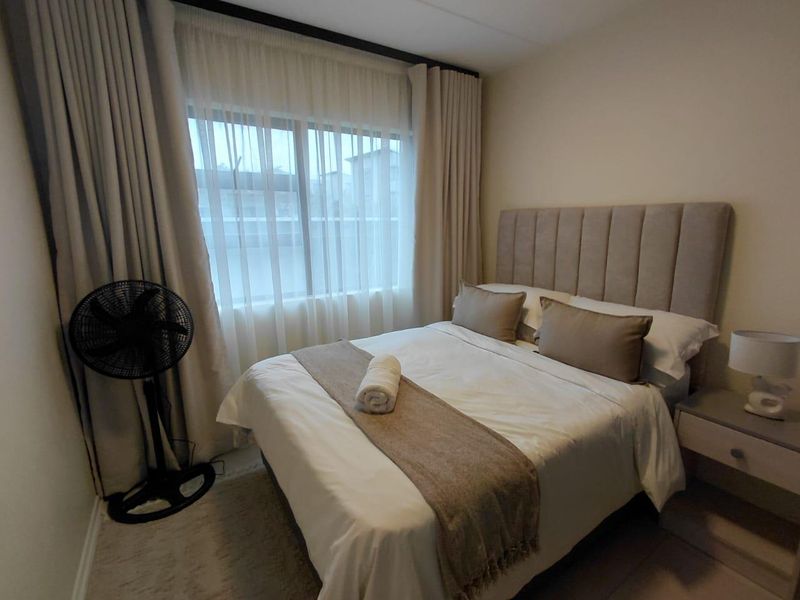 A well-lit bedroom featuring neutral tones, floor-to-ceiling curtains, and a window providing natural light.