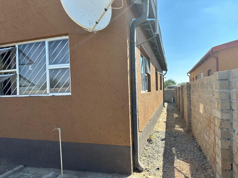 Side view of the property showing the exterior wall, security bars on windows, downpipe, and a boundary wall separating the property from the neighbor.