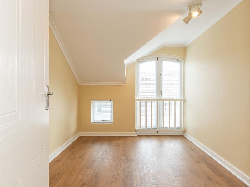 An empty bedroom featuring laminate flooring, a sloped ceiling, and a set of French doors with a small balcony railing.