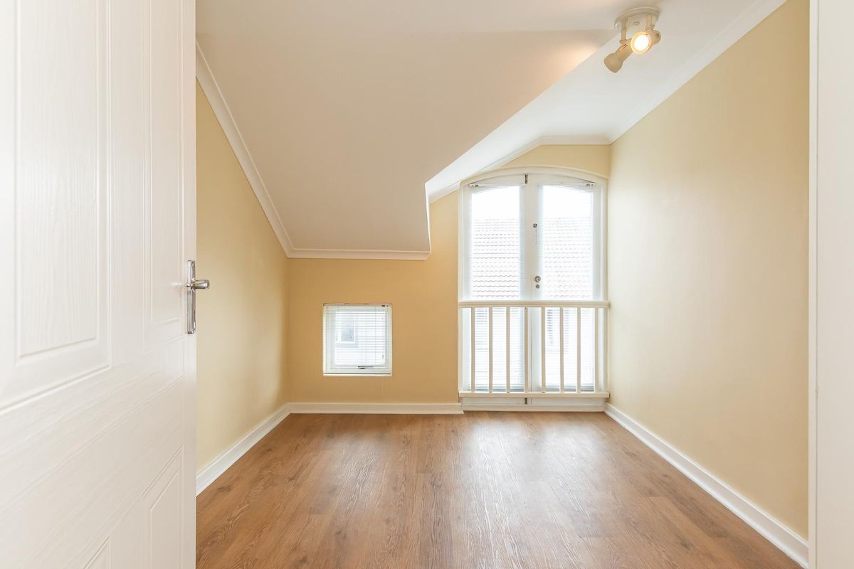 An empty bedroom featuring laminate flooring, a sloped ceiling, and a set of French doors with a small balcony railing.