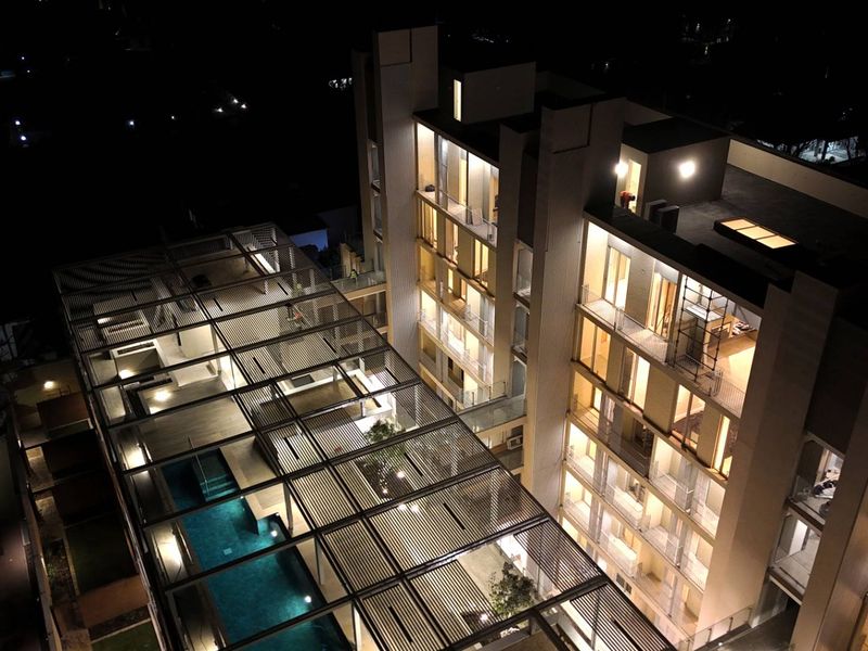 Nighttime aerial view of a modern apartment complex featuring a swimming pool, extensive pergola structures, and illuminated balconies.