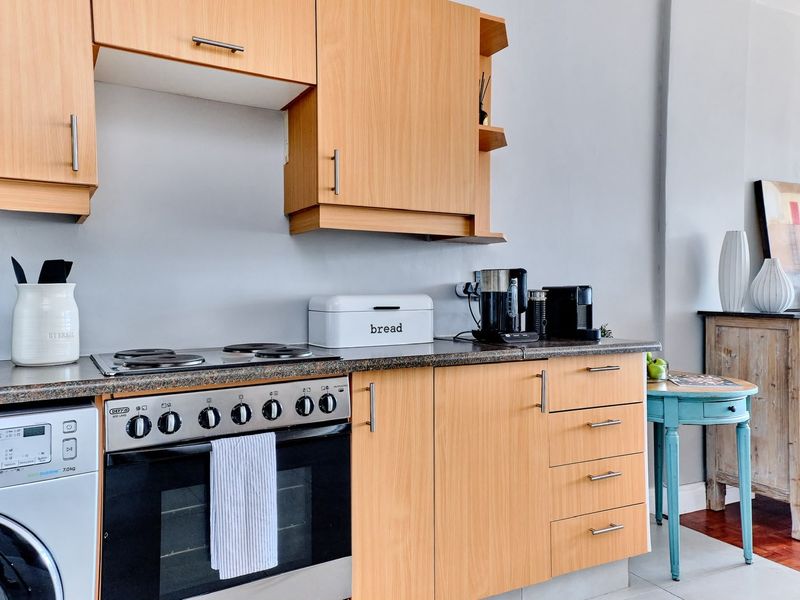 A functional kitchen featuring light wood-finish cabinetry, laminate countertops, and a built-in electric stove with an integrated washing machine.