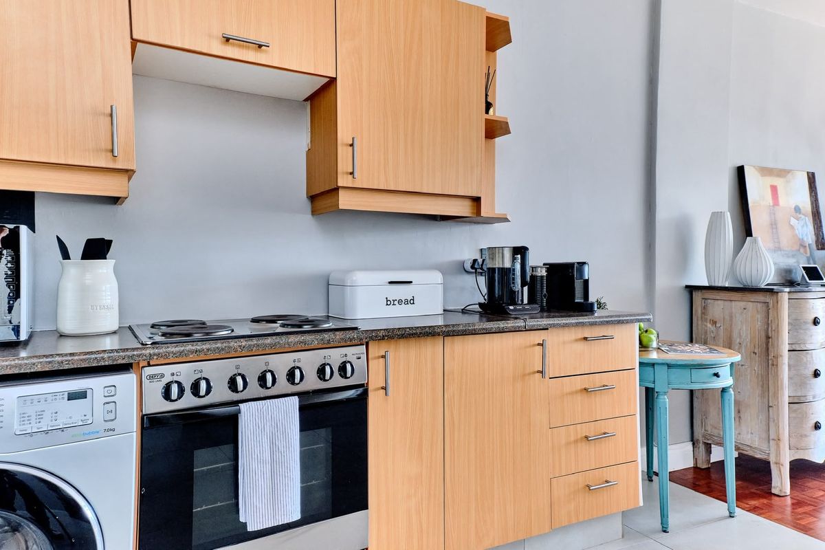 A functional kitchen featuring light wood-finish cabinetry, laminate countertops, and a built-in electric stove with an integrated washing machine.