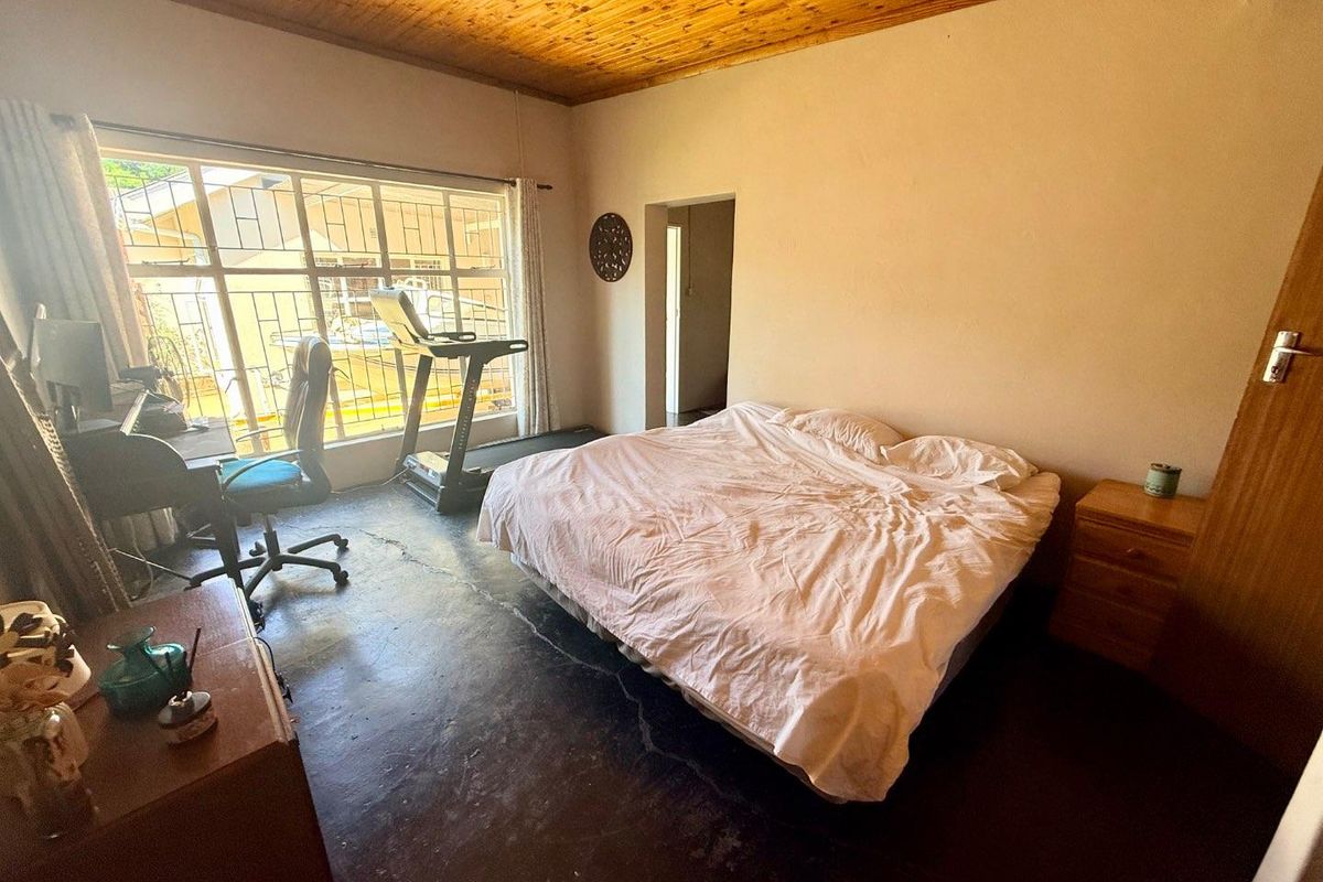 A bedroom featuring a timber-clad ceiling, large window with security bars, and exposed concrete flooring.