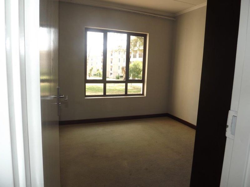 An empty bedroom featuring carpeted flooring and a large window, providing a blank canvas for potential interior design updates.