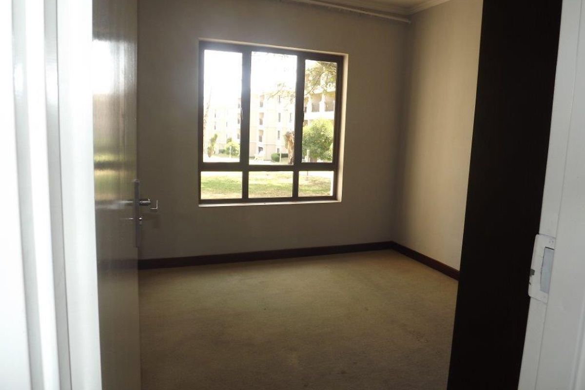 An empty bedroom featuring carpeted flooring and a large window, providing a blank canvas for potential interior design updates.