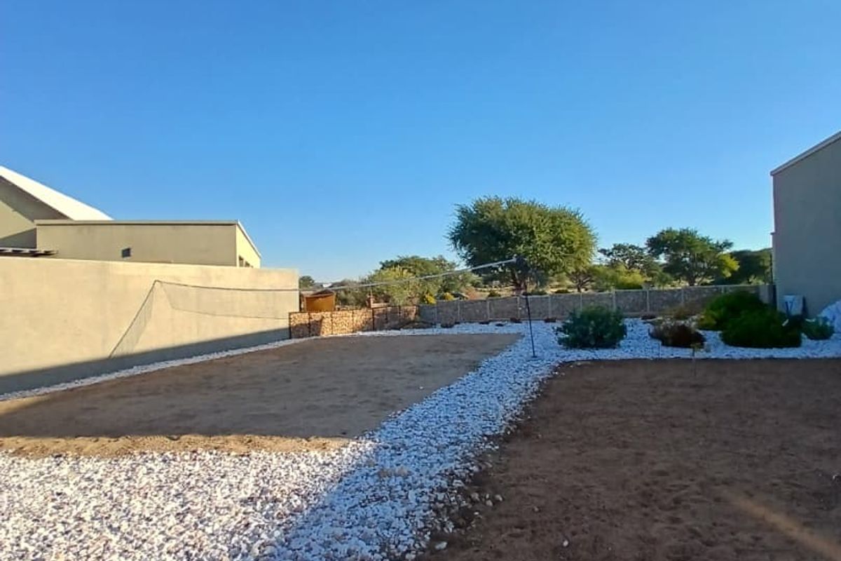 A rear garden area featuring a mix of gravel landscaping and open ground, enclosed by boundary walls and perimeter fencing.