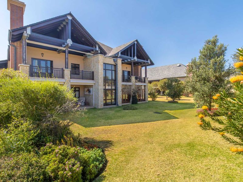 Rear view of a multi-story residence featuring stone cladding, timber balcony structures, and a well-maintained landscaped garden.