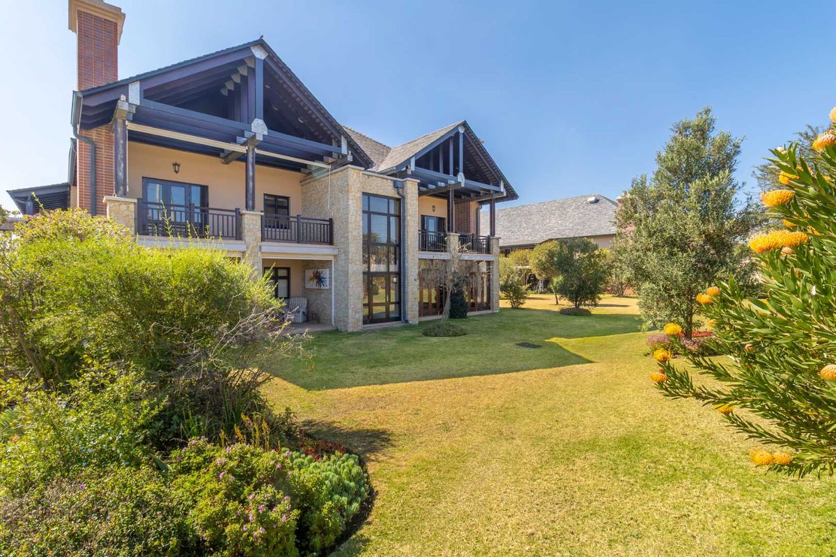 Rear view of a multi-story residence featuring stone cladding, timber balcony structures, and a well-maintained landscaped garden.